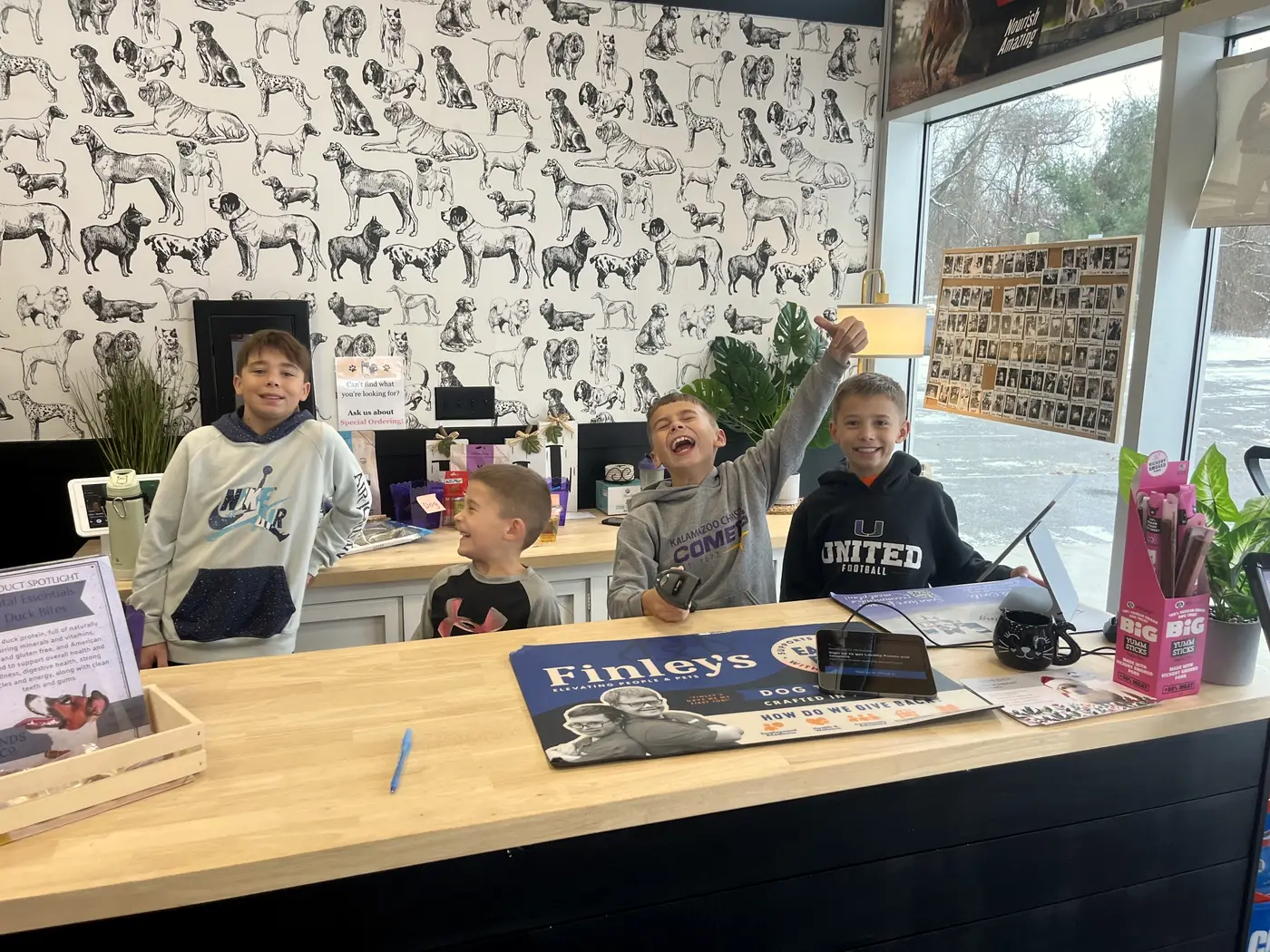 Four boys laughing behind the Portage checkout counter in front of the dog-print wallpaper